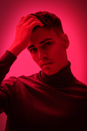An attractive young brunet man posing in a stylish turtleneck on a bright pink background. Men's fashion and style.の写真素材