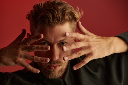 Male beauty. Close up shot of a handsome red-haired man looking  at the camera through his fingers.の写真素材