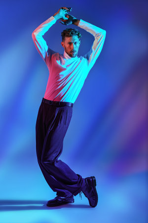 An attractive man in a white turtleneck and black trousers dances a latin dance on a bright blue...
