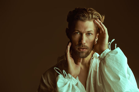 Studio shot of a handsome mature man in a white vintage shirt with wide sleeves on a brown background. Historical portrait, late 19th - early 20th century. Male beauty. Copy space.の写真素材