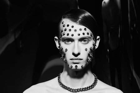 A handsome brunet man with chain and metal spikes on his face posing on a black background. Fashion...