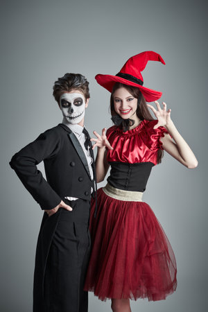 Halloween party for teenagers. Portrait of a teenage boy in a costume of skeleton and a girl in a witch's costume posing together with fun at studio. Grey background with copy space.の写真素材