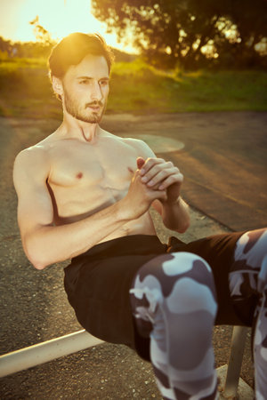 A muscular man with bare torso is doing push-up exercises at the gym in the park at sunset. Outdoor...
