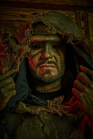 A terrible bearded man with scars on his face, dressed in burlap clothes, looking at the camera with...