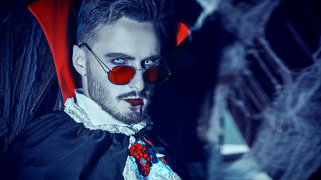 Portrait of a bloodthirsty aristocratic vampire standing in his dark dusty castle with cobweb all around. Halloween. Vampires.の写真素材