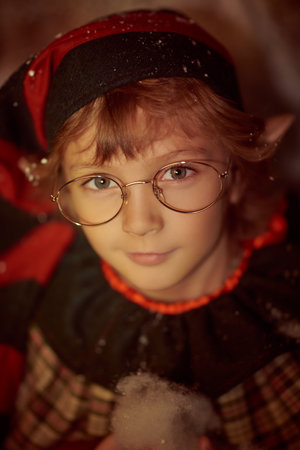 Fairy tale about Christmas. A cute little elf boy stands outdoors at nighttime looking with a smile at the camera. Close up shot. Snowy night.の写真素材