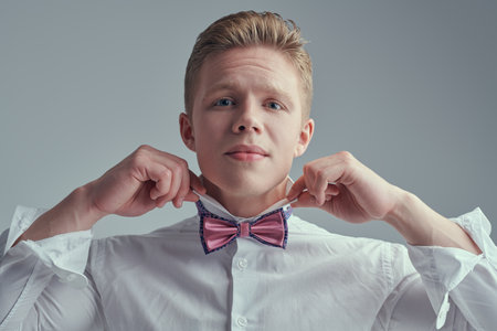 A well-groomed young blond man adjusting the colar of his white shirt. Male fashion and style. Happy people, emotions. White background.の写真素材
