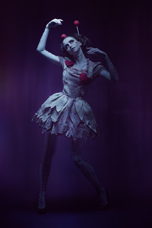 Halloween. Full-length portrait of a pretty girl in a dress and with a make-up and hairstyle of a voodoo doll moving like a puppet on a dark background. Studio shot. Voodoo religion.の写真素材