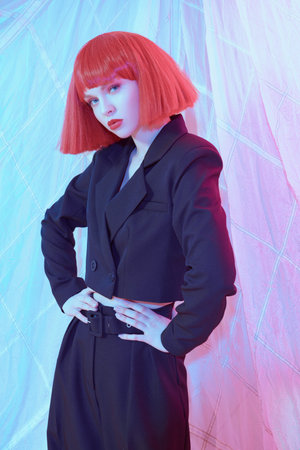 Fashion shot. Beautiful female fashion model with bright red hair poses in fashionable black...