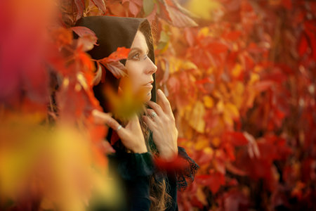 A beautiful shaman woman with long curly hair and ethnic ornaments on her face stands among red foliage in the forest. Fantasy. Ethnic culture. Shaman woman.の写真素材