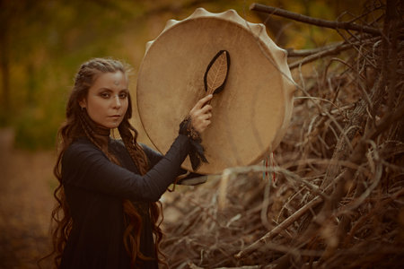 Shamanic rituals. A shaman woman with long curly hair and ethnic ornaments on her face performs a...