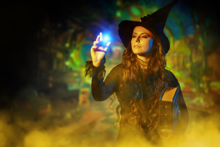 A pretty curly-haired sorceress in a black hat and black dress with a magic book of spells creates a...