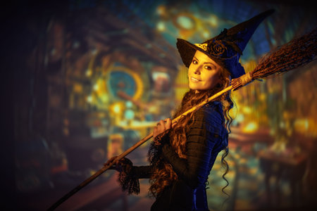 Portrait of a beautiful joyful young witch in a black hat and dress standing on a magical background...
