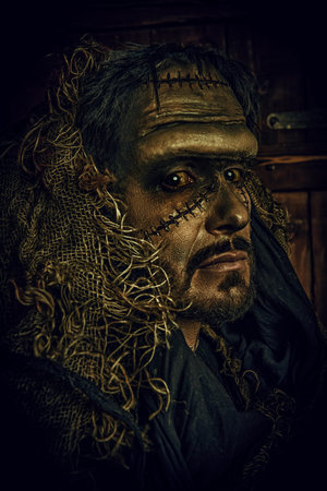 Halloween. A scary bearded man with scars on his face, dressed in burlap clothes, looking at the...