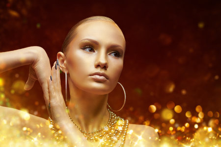 Golden beauty girl. Gorgeous woman with golden make-up and skin wearing golden earrings and necklace on a red background with sparkling golden lights. Copy space. Holiday luxury look. Christmas girl.の写真素材