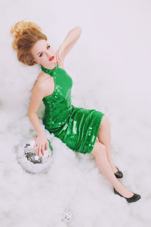 Winter holiday fashion and beauty. Beautiful blonde girl posing in a sparkling green dress in a snowy setting with mirrored disco balls. Christmas and New Year.の写真素材
