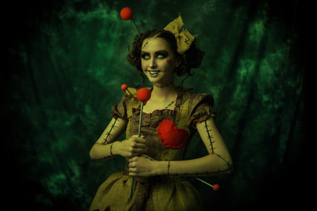 Halloween characters. Attractive girl with make-up, hairstyle and voodoo doll dress smiles cutely and holds a huge pin. Studio portrait on vintage background. Voodoo culture.の写真素材