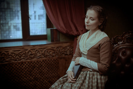 A beautiful aristocratic girl in an 18th century Scottish dress sitting peacefully with a book in a...
