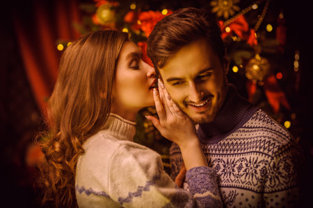 A beautiful girl whispers wishes for Christmas to her beloved young man. Romantic Christmas and New Year.の写真素材