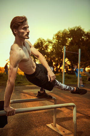 Outdoor sports. A muscular man with bare torso is doing exercises at the gym in the park at sunset....