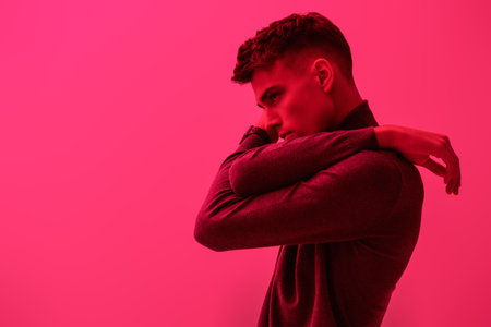 A profile portrait of an attractive young brunet man posing in a  turtleneck on a bright pink background. Men's fashion and style. Copy space.の写真素材