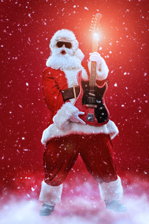 Portrait of cool Santa Claus in sunglasses and headphones playing the guitar and singing. Merry Christmas. Party. Full length shot. Red background with snowfall.の写真素材