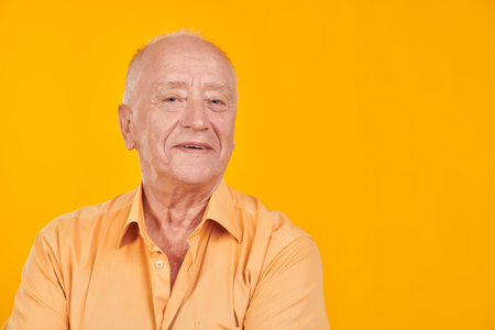 Active and bright senior man in a casual shirt smiles. Elderly people, healthy lifestyle. Yellow background with copy space.の写真素材