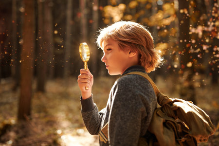 Adventure and wanderlust. An active boy with a backpack observes something with a loupe in a wonderful summer forest.の写真素材