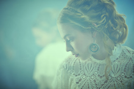 Portrait of a stunning young woman wearing a feminine white dress in 19th century style standing by the mirror in a vintage room filled with haze. Victorian style.の写真素材