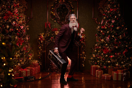 Fashionable party at Christmas and New Year. A modern Santa Claus in an elegant three piece suit dances with a tape recorder in his hand in magical Christmas setting.の写真素材