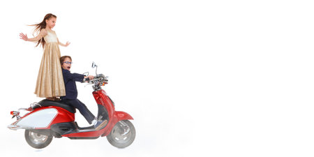 Children's fashion and holidays. Cute little boy and a girl in beautiful evening clothes ride a red scooter. Children's party. White studio background with copy space.の写真素材
