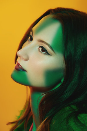 Close up shot of a beautiful brunette woman with elegant make-up on a yellow background in green...