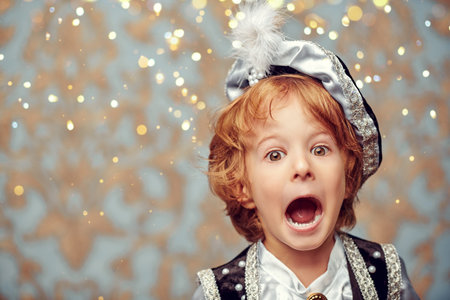 Portrait of a cute little blond boy in a costume of a fairy tale prince joyfully screaming on a...