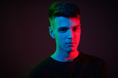Close up shot of a handsome young brunet man looking calmly at the camera. Black background in mixed...