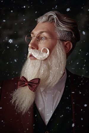A portrait of a handsome Santa Claus with an elegant white beard and mustache in a festive green three-piece suit, a hat and spectacles on a vintage background with snow. Fashion and Christmas, New Year.の写真素材