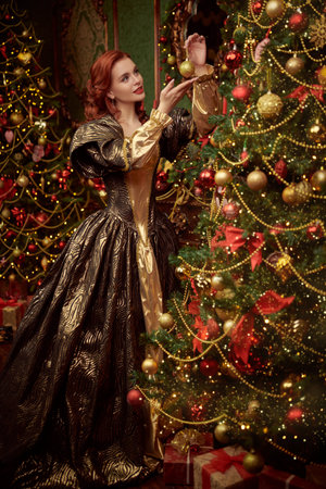 Christmas stories. Beautiful kind princess girl with curly red hair decorates the Christmas trees for Christmas in her castle.の写真素材