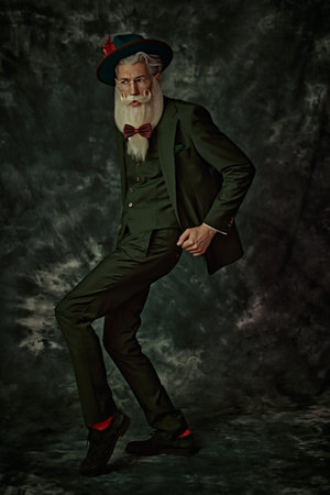 Full-length shot of a handsome Santa Claus with elegant white beard and mustache in a festive green...