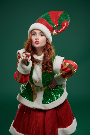 A shot of a merry beautiful Christmas fairy elf girl in a bright costume on a green studio...