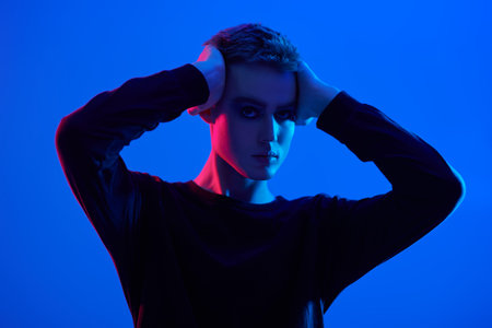Art portrait of a sensual handsome young man posing at studio on a blue background in mixed colored...