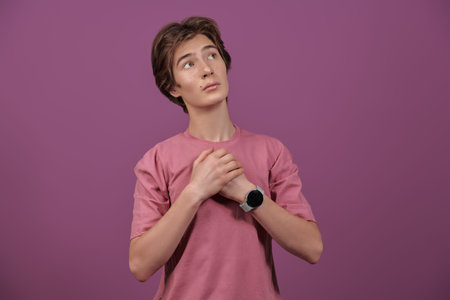 Portrait of a romantic teenage boy pressing his hands to his heart and looks up dreamily. Bright...