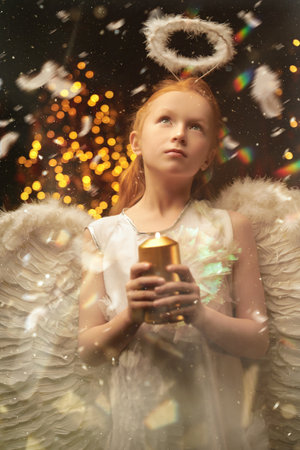 A shot of a little girl wearing a costume of angel holding a candle and dreaming in beautiful Christmas setting. Merry Christmas and Happy New Year!の写真素材