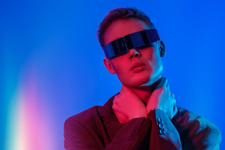 Fashion concept. Portrait of a stylish young man posing in mirrored futuristic glasses in mixed neon...