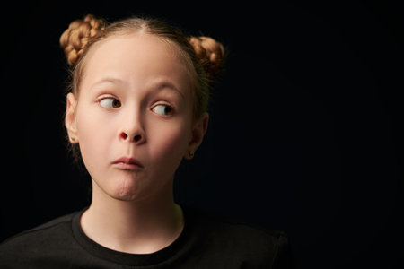 Portrait of a beautiful funny girl in a black t-shirt on a black studio background with copy space. Children, emotions. Psychological picture.の写真素材