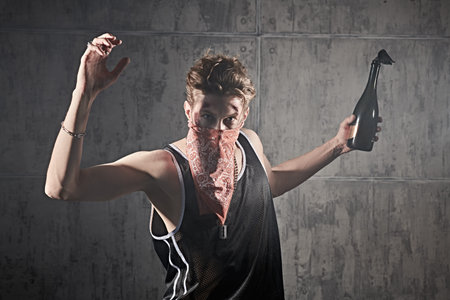 An aggressive determined man with wounds on his face and the bandana covering his face raises a...