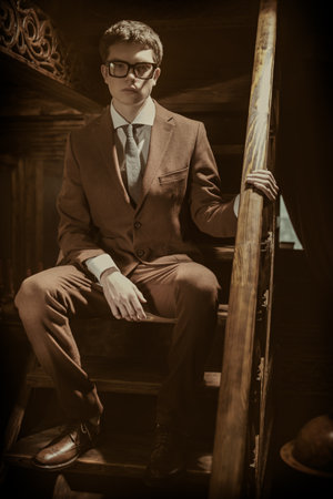 A full-length portrait of a handsome young man in a formal suit and stylish spectacles posing in a luxury apartments with classic interior. Men's fashion. Clothes and accessories.の写真素材