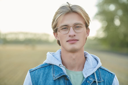 Denim fashion. Portrait of a handsome smiling man in denim jacket and stylish glasses against an...