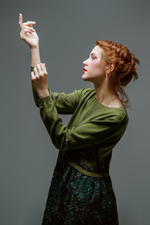 Adorable red-haired girl fashion model with delicate make-up and curly red hair poses in an olive dress on a gray studio background. Fashion and beauty portrait.   Makeup and cosmetics, hairstyle.の写真素材
