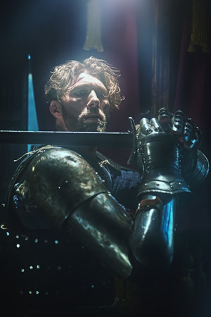 A handsome noble medieval knight in armor stands with a raised sword in a castle surrounded by haze. A scene from a chivalric romance. Historical reconstruction.の写真素材