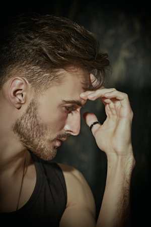 Sideview portrait of a handsome young brunet man of athletic build posing in a black tank top against a concrete wall . Masculinity and male beauty.の写真素材