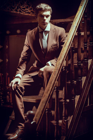 A full-length portrait of a handsome young man in a formal suit and stylish spectacles posing in a luxury apartments with classic interior. Men's fashion. Clothes and accessories.の写真素材